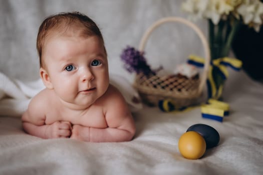 Cute little baby on Easter. Yellow and blue easter eggs are nearby. She looks at the camera and smiles. Ukraine. The concept of peaceful Easter. High quality photo