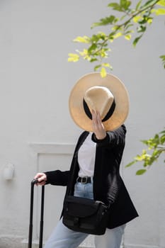 young happy brunette girl in sunglasses and straw hat with a suitcase goes on vacation, a woman stands against the background of a white brick wall, High quality photo