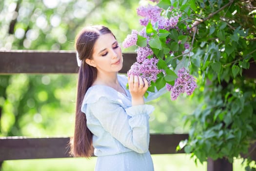 romantic beautiful girl with long hair , in light blue dress stands with lilac flowers, in the garden, in sunny day. Close up. copy space