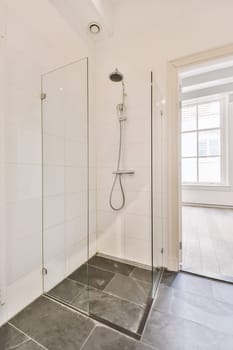 a white bathroom with black tile flooring and shower stall in the corner, there is a large window on the wall