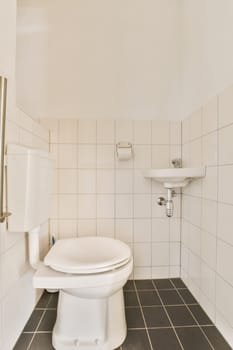 a white toilet in a bathroom with black tiles on the floor and wall behind it is an open shower stall