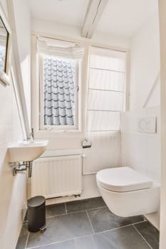 a bathroom with a toilet, sink and window in the corner next to it is a black trash can on the floor