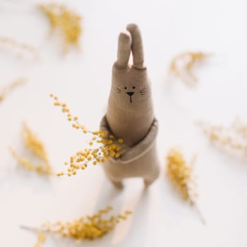 Funny handmade bunny rabbit toy with yellow mimosa flowers. Easter gift concept