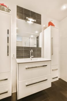 a modern bathroom with white cabinets and black tile flooring on the wall behind it is a large mirror above the sink
