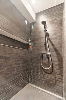 a shower with gray tiles on the walls and floor, in a modern style bathroom area that is well lit by natural light
