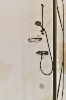a bathroom with white tiles and black shower faucets on the wall next to the bathtub is a hand held by a