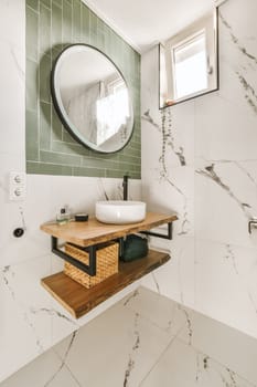 a modern bathroom with marble tiles and green tile walls, including a round mirror on the wall above the sink