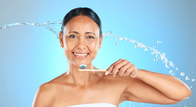 Dental, health and woman brushing teeth with toothbrush, toothpaste and water splash on blue studio background. Healthcare, self care product and oral care hygiene of mature Brazilian beauty model
