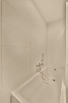 a bathroom with white tiles on the walls, and a shower head in the corner of the bathtub is attached to the wall