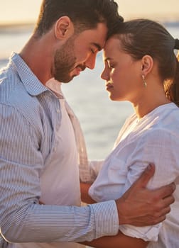 Couple, sunset and beach for love together on holiday or honeymoon. Man, woman and ocean in embrace for romance, during vacation, trip or travel by the sea in late summer sunlight show happiness.