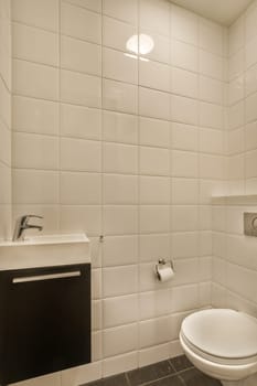 a bathroom with white tiles on the walls and black tile flooring around the toilet in front of the sink