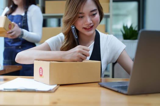 Starting small business entrepreneur of independent Asian woman smiling using computer laptop with cheerful success of online marketing package box items and SME delivery concept.