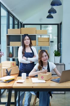 Starting small business entrepreneur of independent Asian woman smiling using computer laptop with cheerful success of online marketing package box items and SME delivery concept.