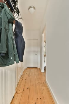 a hallway with wooden flooring and clothes hanging from the ceiling to the left side of the room, there is a coat rack
