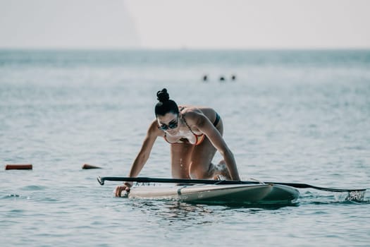 Sea woman sup. Silhouette of happy middle aged woman in rainbow bikini, surfing on SUP board, confident paddling through water surface. Idyllic sunset. Active lifestyle at sea or river