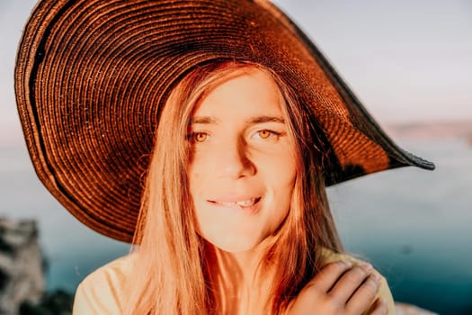 Portrait of happy young woman wearing summer black hat with large brim at beach on sunset. Closeup face of attractive girl with black straw hat. Happy young woman smiling and looking at camera at sea