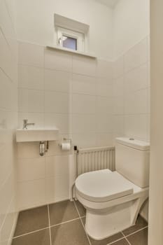 a toilet in a bathroom with white tiles on the floor and wall behind it is a window that looks out to the outside