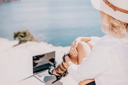 Happy girl doing yoga with laptop working at the beach. beautiful and calm business woman sitting with a laptop in a summer cafe in the lotus position meditating and relaxing. freelance girl remote work beach paradise