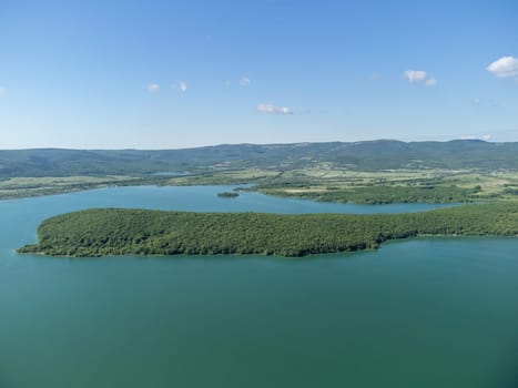 Aerial landscape from flying drone storage reservoir at mountain foot covered colorful spring forest. Beautiful view from above blue lake among highlands