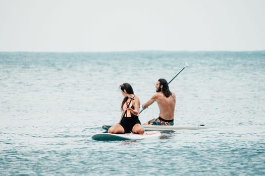Sea woman and man on sup. Silhouette of happy young woman and man, surfing on SUP board, confident paddling through water surface. Idyllic sunset. Active lifestyle at sea or river