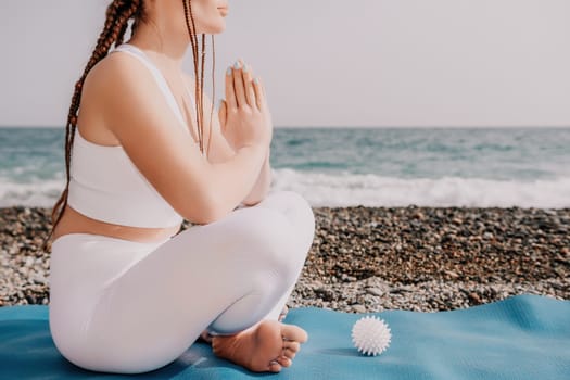 Woman yoga sea. Young woman with braids dreadlocks in white swimsuit and boho style braclets practicing outdoors on yoga mat by the ocean on sunny day. Women's yoga fitness routine. Healthy lifestyle, harmony