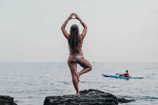 Woman meditating in yoga pose silhouette at the ocean, beach and rock mountains. Motivation and inspirational fit and exercising. Healthy lifestyle outdoors in nature, fitness concept.