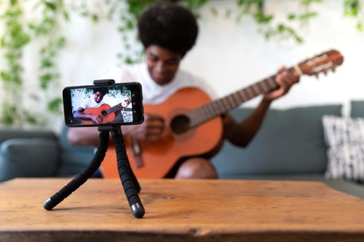 Young african american man recording a guitar lesson with his cellphone. Selective focus on phone. E-learning concept.