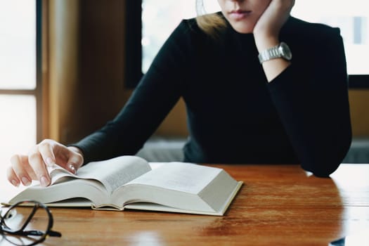 A portrait of a young Asian woman reading textbooks shows boredom on a wooden desk in library..