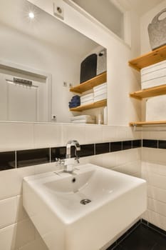 a bathroom with black and white tiles on the walls, shelves above the sink basin bowl is in front of the mirror