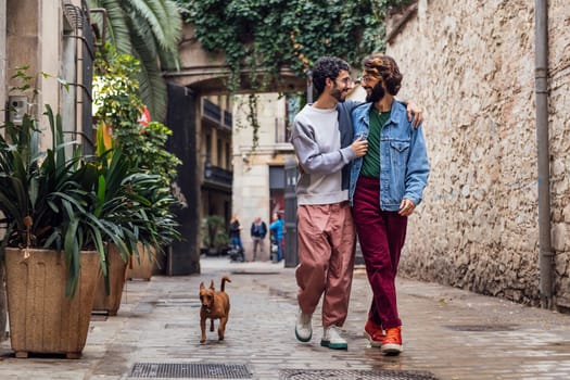 gay male couple walking with their dog along a beautiful cobbled street decorated with plants, concept of leisure and love between people of the same sex