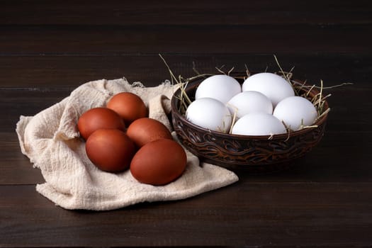 Raw white chicken eggs dyed for Easter with onion skins lie in a glossy bowl and on a napkin on the surface of their natural dark wood. Healthy food. Dark key, rustic.
