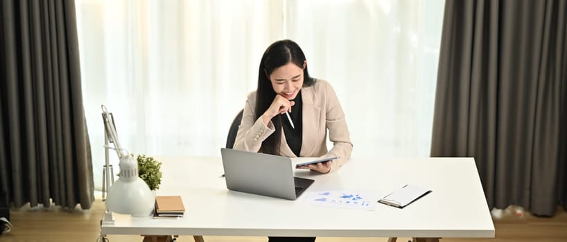 Above view of asian woman corporate CEO in elegant suit working with laptop computer at modern workplace.