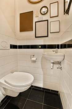 a bathroom with black and white tiles on the floor, mirror above the toilet bowl, and framed pictures hanging on the wall