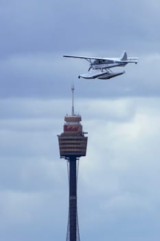 A striking portrait photo of a seaplane flying next to the iconic Sydney Westfield tower on a cloudy day. Perfect for advertising, editorial content, or art for aviation enthusiasts and city lovers.