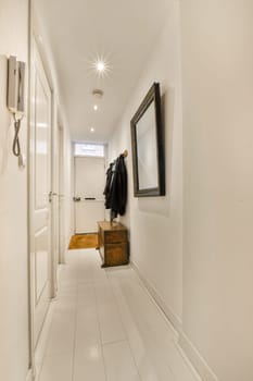 a long hallway with white tile flooring and an open door leading to another room on the wall is framed by a coat rack