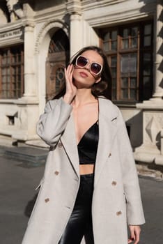 Street style, autumn, spring fashion concept: fashionable woman wearing luxury beige coat, a top with razors and sunglasses