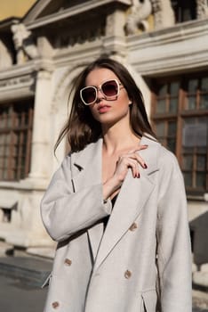 Street style, autumn, spring fashion concept: fashionable woman wearing luxury beige coat, a top with razors and sunglasses