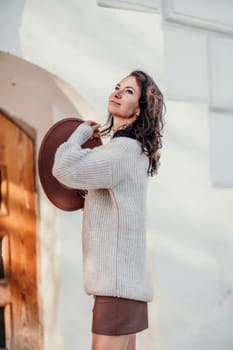 Woman walks in the city, lifestyle. Young beautiful woman in a loose light sweater, brown skirt and sneakers with a hat