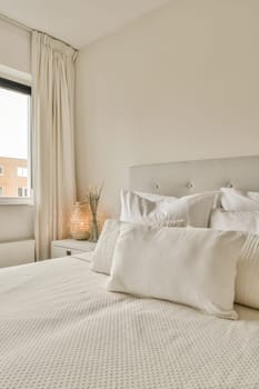 a bed with white sheets and pillows in a small room next to a window that is lit by the sun