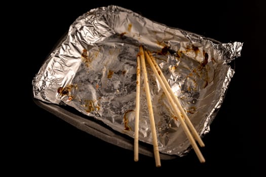 An empty plastic container for the delivery of a set of sushi. Chopsticks and an empty thermobox with foil inside for a set of sushi on a dark background. lunch. top side view. Flat lay. Copy space