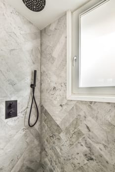 a modern bathroom with marble tiles and black shower faucet in the corner of the shower stall is next to the window