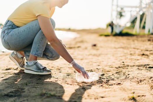 Young female volunteer satisfied with picking up trash, a plastic bottles and coffee cups, clean up beach with a sea. Woman collecting garbage. Environmental ecology pollution concept. Earth Day.