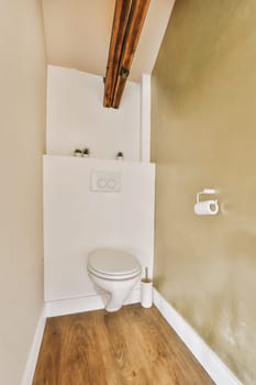 a toilet in the corner of a room with wood flooring and walls painted white, there is a light fixture on the wall