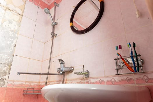 an old dirty shabby bathroom with fallen tiles. an old ruined bathroom. the sink and mixer are visible. mirror