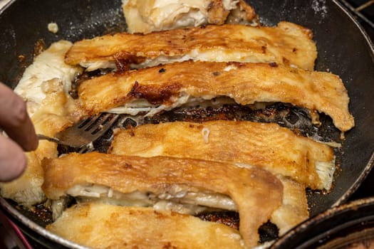 the cook checks the readiness of the fish with a fork. delicious pieces of fried flounder in a frying pan. Cooking fish. Supper. Healthy eating. Seafood