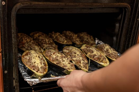 the hostess puts a baking tray with eggplant stuffed with meat in the oven. Eggplant halves stuffed with minced meat, spices and cheese, for baking in the oven. Delicious and healthy food