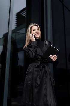 a business woman holds a phone in her hand and speaks with a partner on a cellular connection against the backdrop of a business center.