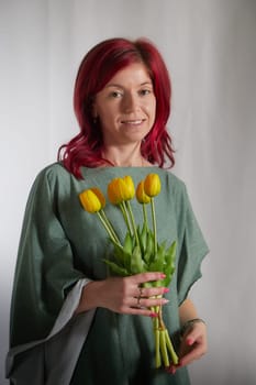 Beautiful woman with red hair in yellow dress on light background holds tulips. Inernational woman's day 8 March