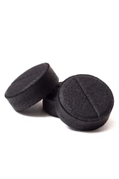Three black charcoal tablets isolated on a white background close up