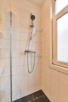 a shower room with white tiles and black flooring on the walls, there is a window in the corner